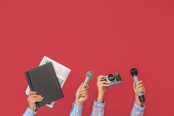 Female hands with microphones, photo camera, notebook and newspaper on color background