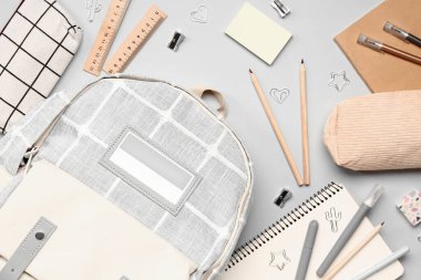 Gri arka planda farklı kırtasiye malzemeleriyle süslü okul çantası.