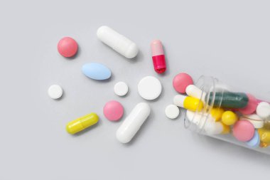 Gri arka planda farklı haplarla çevrilmiş şişe, yakın plan.