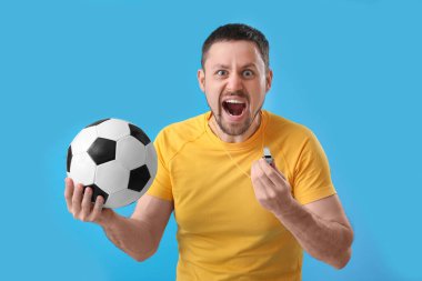 Futbol topu ve mavi arka planda ıslık çalan kızgın erkek koç.