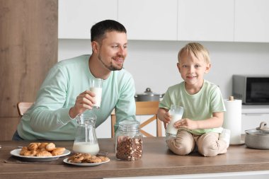 Mutlu küçük çocuk ve babası farklı hamur işleriyle mutfakta süt içiyorlar.