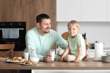 Mutlu küçük çocuk ve babası farklı hamur işleriyle mutfakta süt içiyorlar.