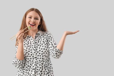 Lezzetli suşi rulosu olan genç bir kadın gri arka planda bir şey gösteriyor.