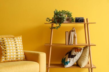 Sarı duvarın yanında rahat bir koltuk ve raf ünitesi.