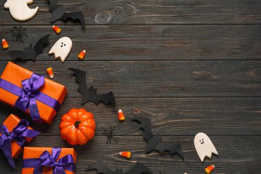 Hediye kutuları, lezzetli mısır şekerlemeleri, kurabiyeler ve koyu ahşap arka planda Cadılar Bayramı dekoru.