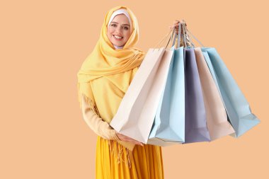 Soluk turuncu arka planda alışveriş torbalarıyla tesettürlü güzel, mutlu bir kadın.
