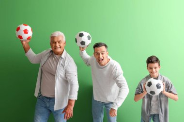 Babası ve büyükbabasıyla küçük bir çocuk yeşil arka planda futbol topları tutuyor.
