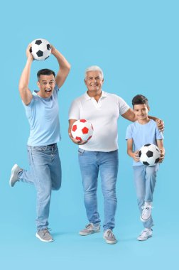 Babası ve büyükbabasıyla küçük bir çocuk mavi arka planda futbol topları tutuyor.