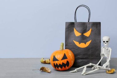 Alışveriş çantası, balkabağı ve iskelet gri ahşap masada. Cadılar Bayramı konsepti