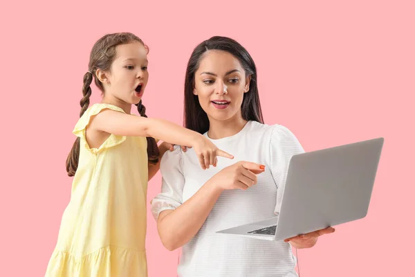 Working mother with her little daughter pointing at laptop on pink background