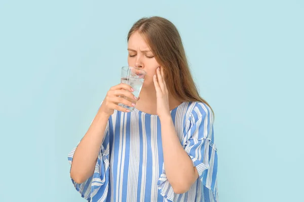 青い背景に冷たい水を飲んでいる敏感な歯を持つ若い女性 — ストック写真
