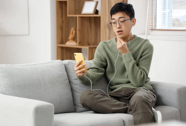 Young Asian man with mobile phone video chatting at home