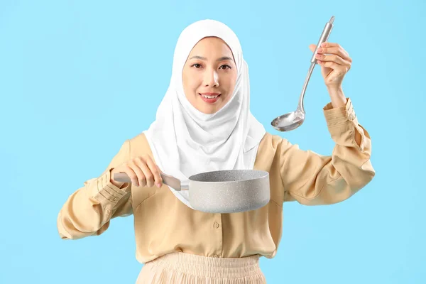青い背景にソースパンと梯子を持つヒジャブの若いアジアの女性 — ストック写真