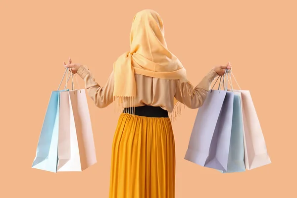 Young beautiful happy woman in hijab with shopping bags on pale orange background, back view