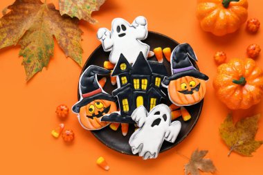 Farklı lezzetli kurabiyeler, kuru yapraklar ve balkabağı ile Cadılar Bayramı kutlaması için turuncu arka planda.