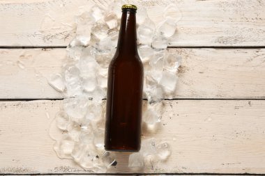 Beyaz ahşap arka planda bir şişe soğuk bira ve buz.