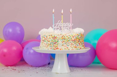 Balonlar ve leziz doğum günü pastasıyla pembe duvarın yanındaki masada dur.