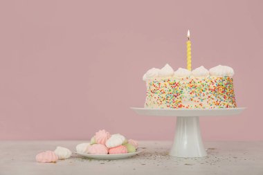 Lezzetli doğum günü pastası ve pembe duvarın yanındaki masada kremalı pastayla dur.