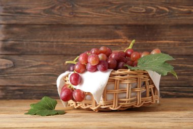 Tahta arka planda lezzetli olgun üzümlerle dolu hasır bir kase.