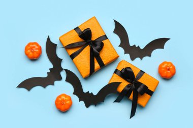 Cadılar Bayramı partisi için balkabaklı kağıt yarasalar ve mavi arka planda hediye kutuları.