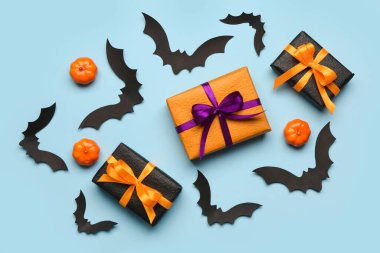 Cadılar Bayramı partisi için balkabaklı kağıt yarasalar ve mavi arka planda hediye kutuları.