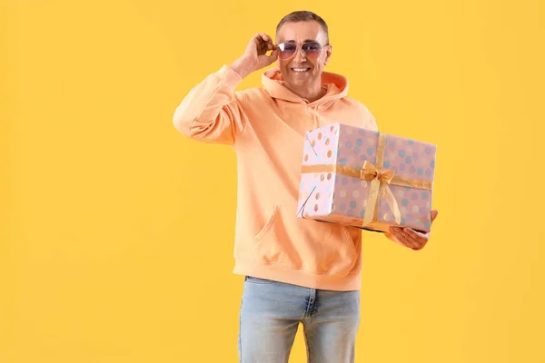 Mature man with birthday gift on orange background