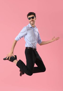 Pembe arka planda atlayan takım elbiseli genç adam.