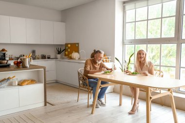 Olgun bir çift mutfakta yemek yiyor.