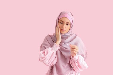 Sorunlu, pembe arka planda hamilelik testi olan tesettürlü genç bir kadın.