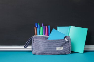 Tahtanın yanındaki mavi masada farklı okul kırtasiyesi olan kalem kutusu.