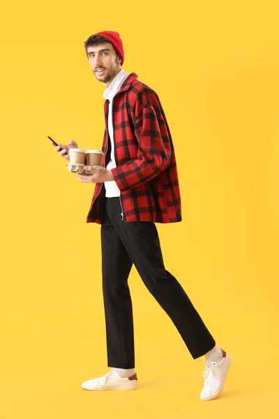 Przystojny Młody Człowiek Filiżankami Kawy Przy Użyciu Telefonu Komórkowego Żółtym — Zdjęcie stockowe