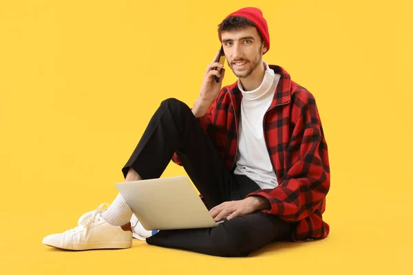 Przystojny Młody Człowiek Laptopem Rozmawiający Przez Telefon Komórkowy Żółtym Tle — Zdjęcie stockowe