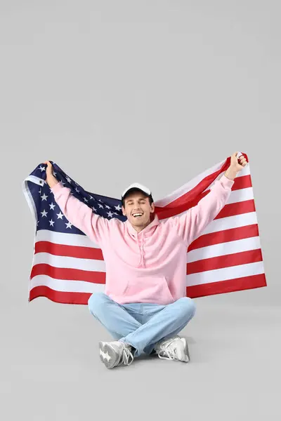 Young man with USA flag sitting on light background