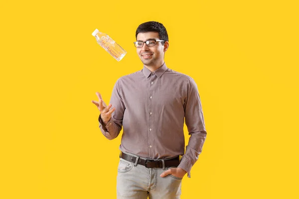 年轻人在黄色的背景上扔瓶子水 — 图库照片
