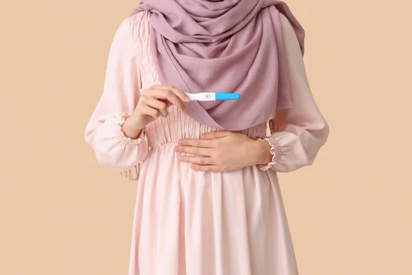 ベージュの背景で肯定的な妊娠テストを持つムスリム女性 — ストック写真