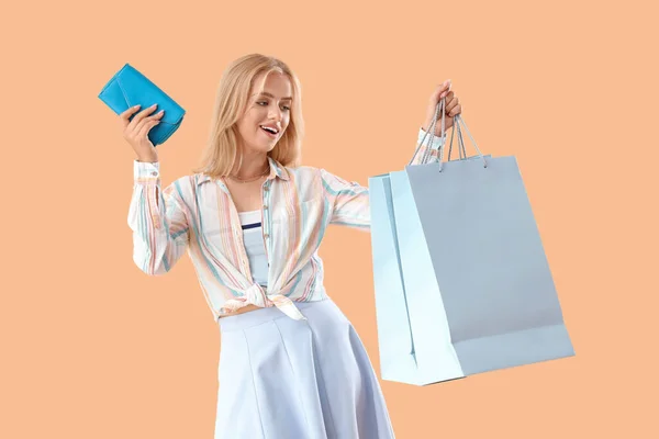 Beautiful young woman with shopping bags and wallet on orange background