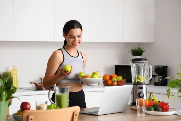 Sporty young woman with apples and laptop in kitchen