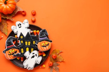 Farklı lezzetli kurabiyeler, kuru yapraklar ve balkabağı ile Cadılar Bayramı kutlaması için turuncu arka planda.