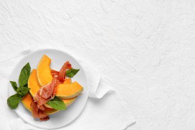 Hafif arka planda lezzetli kavun, jambon ve fesleğen tabağı.