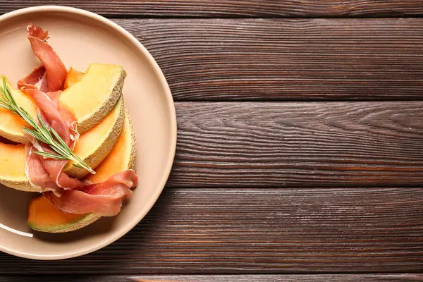 Plate with tasty melon and prosciutto on dark wooden background