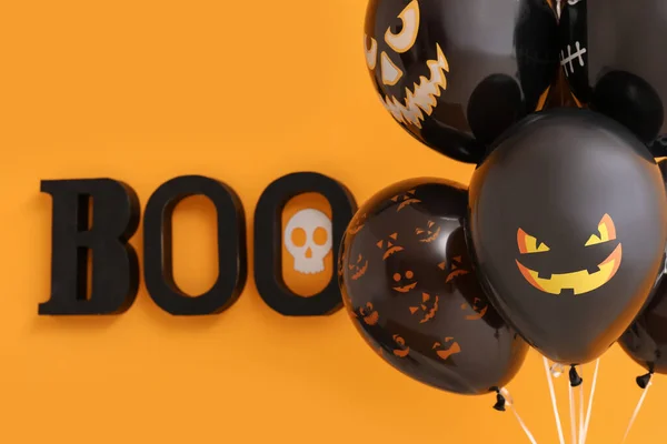 Different black Halloween balloons and text BOO hanging on orange wall in room, closeup
