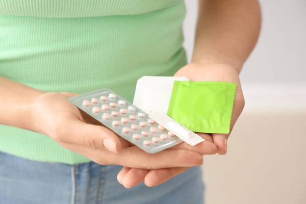 Young woman with contraceptives on light background, closeup