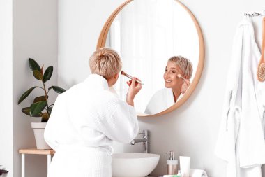 Banyoda aynanın yanında makyaj yapan olgun bir kadın.