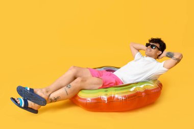 Sarı arka planda duran şişme yüzüklü genç adam.