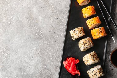 Gri arka planda lezzetli suşi ruloları, zencefil ve çubuklarla dolu tabak.