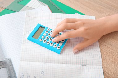 Ahşap masada hesap makinesiyle çalışan kadın, yakın plan.