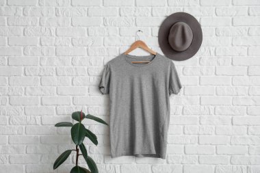Beyaz tuğla duvarda asılı şık gri tişört ve şapka