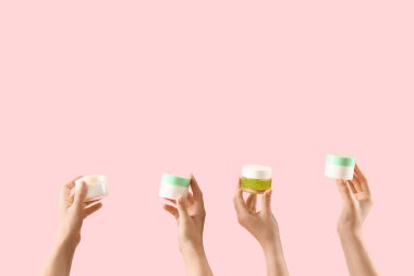 Pembe arka planda kozmetik krema kavanozları tutan kadın elleri