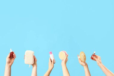 Mavi arka planda farklı kozmetik ürünleri tutan kadın elleri