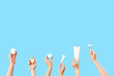 Mavi arka planda farklı kozmetik ürünleri tutan kadın elleri